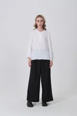 Blusa blanca de poliéster, entallada, con escote en V y botones frontales. Presenta mangas largas con puños anchos.