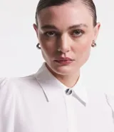 Camisa blanca de crepé con cuello solapa, abotonada, mangas largas abullonadas y sin estampado.
