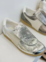 Zapatillas deportivas plateadas con detalles en color crema y suela color caramelo.