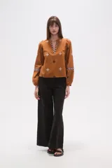 Blusa de algodón color tostado con bordados geométricos en blanco y azul marino, cuello mao con escote en V y mangas largas abullonadas con puños elásticos.