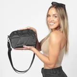 Cartera bandolera color beige con diseño acolchado y correa larga negra regulable.