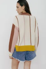 Buzo tipo polo de punto con rayas verticales en tonos beige, marrón y rosa. Tiene cuello polo marrón, cierre parcial con botones amarillos y terminaciones acanaladas en puños y ruedo.