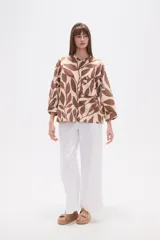 Camisa holgada con estampado de hojas en tonos marrones y beige, cuello mao, cierre frontal con botones y un bolsillo en el pecho.