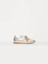 Zapatilla plateada de cuero vacuno con recortes en cuero descarne, doble cordón (uno blanco y otro marrón con pintitas) y charms colgantes.