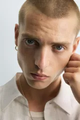 Camisa blanca de manga corta con cuello solapa y textura jacquard irregular. Corte relajado (relaxed fit) con aberturas laterales y cierre frontal de botonadura.