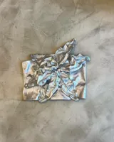 Top de cuero genuino plateado, diseñado con técnica "zero waste". Presenta una estructura maleable y ajustable con un gran nudo central que simula una flor y espalda regulable.