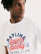 Camiseta blanca de algodón con cuello redondo y mangas cortas. Estampa rectangular con borde negro que contiene la frase "NATURAL ATMOSPHERE" en letras mayúsculas y una imagen de montañas y mar.