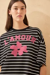 Vestido corto a rayas horizontales blancas y negras, con cuello redondo y mangas cortas. Presenta un estampado frontal con la palabra "L'AMOUR" en rojo y una flor roja. Tiene un tajo lateral en el ruedo.