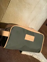 Neceser de lona verde con detalles en cuero color beige y etiqueta con logo de la marca Sierra Mora.