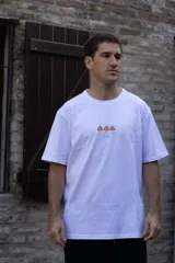 Remera blanca de manga corta con cuello redondo y estampado de tres hongos rojos y la palabra "Tuya" en el frente.