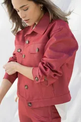 Campera color ladrillo de jean elastizado, corte cropped, con cuello camisero, cierre frontal con botones carey, bolsillos de parche con botón en el pecho y puños abotonados.