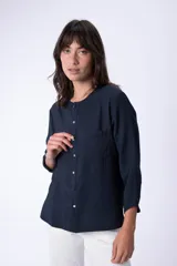 Blusa blanca de manga larga con cuello redondo, detalle de bolsillo y botones frontales.