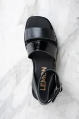 Sandalias negras de cuero con plataforma y dos tiras sobre el empeine, una de cuero liso y otra charolada. La tira del tobillo es de cuero con textura tipo cocodrilo y hebilla metálica.