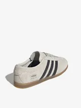 Zapatillas Adidas Gazelle Lo Pro color gris claro con las tres tiras laterales en negro y suela de goma color caramelo.