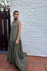 Vestido largo verde oliva de tela simil agamuzada, con escote halter, espalda baja y volados en cuello y cadera.