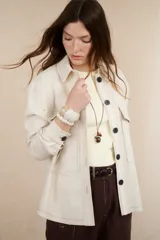 Sobrecamisa color beige de lino con cuello camisero, cierre frontal con botones negros, mangas largas con puños abotonados, dos bolsillos de parche en el pecho y dos bolsillos laterales.