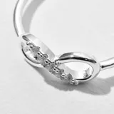 Anillo plateado con forma de infinito y pequeños cristales incrustados.