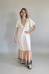 Vestido largo color crema, con escote en V, mangas cortas y falda con volados en color rosa y estampado abstracto.