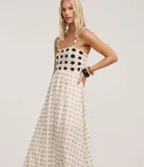 Vestido midi de algodón, color crema, con breteles finos. El corpiño presenta un diseño de crochet con motivos florales en azul marino, y la falda evasé tiene un estampado de pequeños íconos abstractos en azul.