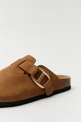 Zuecos negros con base de corcho, puntera cerrada y hebilla dorada decorativa.