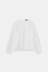 Camisa blanca de cuello redondo con detalle de nido de abeja y entredoses. Manga larga con bordados a tono y cierre trasero con botones.