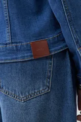 Campera clásica de jean color azul medio, con cuello clásico, cierre frontal con botones, bolsillos con solapa en el pecho y mangas largas con puños abotonados.