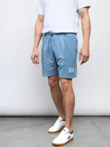 Bermuda deportiva celeste de felpa sin friza con efecto lavado, cintura elastizada con cordón ajustable y logo de la marca Umbro estampado en blanco en la pierna izquierda.