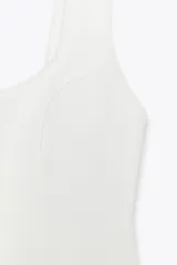 Top blanco de escote pico y tirantes anchos con detalle de picueta a tono y abertura en el bajo.