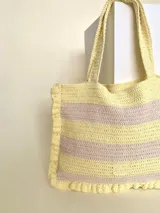 Bolso tipo tote tejido a crochet, con hilo 100% algodón, a rayas horizontales color crema y lila, con volados en los bordes y manijas reforzadas.