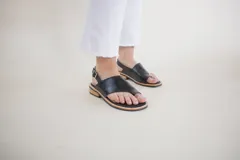 Sandalias de cuero negro con tira entre los dedos, talón descubierto y hebilla lateral.