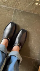 Mules de cuero color marrón con punta cuadrada y detalle de tachas doradas.