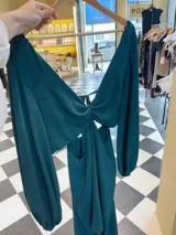 Vestido largo color verde esmeralda, con mangas largas abullonadas, escote con aro central y falda con capas. Espalda descubierta con lazos ajustables.