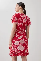 Vestido corto cruzado de color rojo con estampa floral blanca, con volados en el ruedo y lazo para ajustar en la cintura.