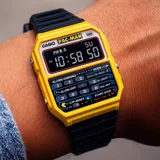 Reloj digital Casio con carcasa de resina amarilla y correa de resina negra. Presenta una pantalla digital con hora, día de la semana y segundos, y un panel inferior con botones funcionales que simulan un teclado numérico y controles de cronómetro, con gráficos alusivos al videojuego Pac-Man.