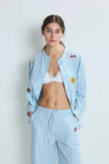 Conjunto de pijama celeste a rayas verticales blancas, compuesto por una camisa de manga larga con cuello mao y botones, y un pantalón de corte recto. La camisa y el pantalón tienen bordados de corazones, soles y otros motivos.