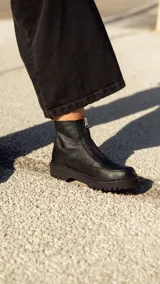 Bota de cuero negra con plataforma, caña baja y cierre frontal con cremallera.