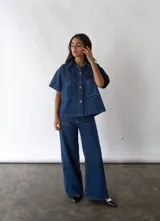 Camisa de denim azul de algodón reciclado, corte amplio, con cuello clásico, manga corta, cierre frontal con botones y dos bolsillos de parche en el pecho.