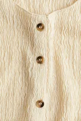 Chaleco color crema de punto texturizado con cuello redondo y botones frontales.