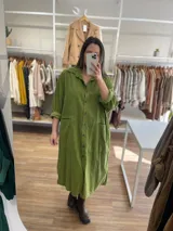 Vestido oversize color verde oliva, de pana fina, con cuello camisero, cierre frontal con botones, mangas cortas con puños arremangados y bolsillos laterales.