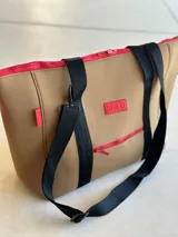 Bolso tote de neopreno negro con cierre superior y bolsillo externo con cierre verde. Tiene asas de mano marrones con bordes naranja, bolsillo interno y monedero haciendo juego.