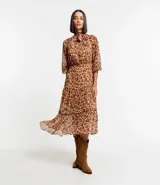 Vestido largo de chiffon con estampa de corazones con diseño de leopardo. Tiene cuello alto con lazo, mangas largas ligeramente transparentes y falda con volado. El tejido contiene hilo metalizado.