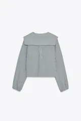 Camisa de manga larga con puños elásticos y cuello bobo con volantes. Cierre frontal con botones.