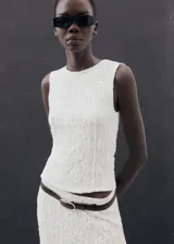 Falda midi de encaje blanco con diseño recto y bajo asimétrico con terminaciones en pico. Posee forro interior y cintura elástica.