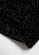 Blusa negra de terciopelo con estampado floral, diseño asimétrico de un solo hombro, manga larga abullonada y detalle de flor en el cuello.