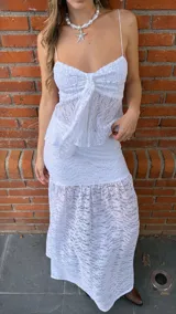 Pollera larga de encaje blanco con volados en el ruedo. Tiene un top a juego con breteles finos y volados en el busto, con un lazo en el centro.