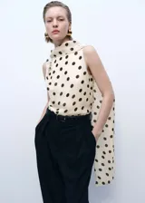 Blusa sin mangas color crema con estampado de lunares marrones, cuello alto con detalle de pañuelo y cierre de botón en la parte posterior.