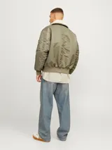 Campera bomber color verde oliva, de manga larga y cuello extendido. Tiene puños ribeteados, cierre con cremallera, bolsillo en la manga y bolsillos frontales con cierre de botón.