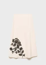 Falda midi color crema, de tiro alto y corte recto. Presenta bordado de flores negras en el lateral inferior.