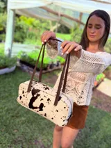 Cartera baguette de cuero color crudo con manchas negras, forro interno de tela y correa de cuero marrón.