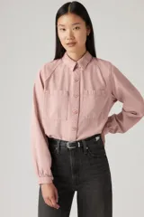 Camisa color rosa pálido, de corte cropped, con cuello camisero, cierre frontal con botones, mangas largas abullonadas con puños elásticos, dos bolsillos de parche en el pecho y canesú en la espalda.